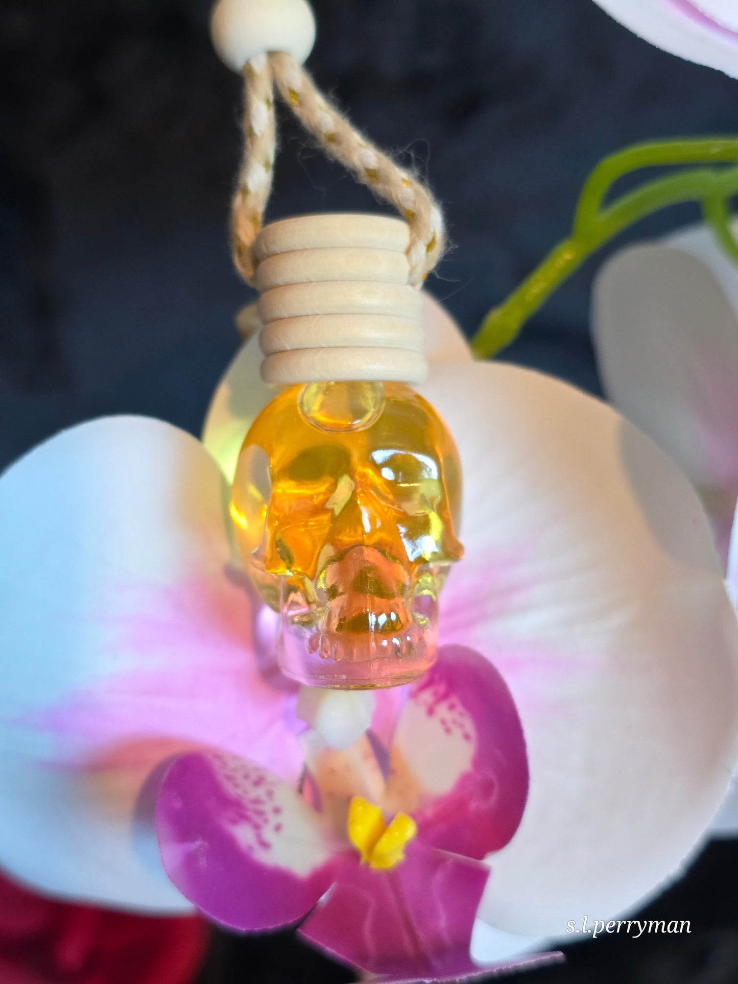 Skull Car Diffuser air freshener sitting on a pink and white flower by Grim Temptations.
